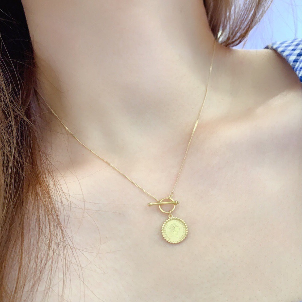 Gold necklace with a round pendant worn by a person