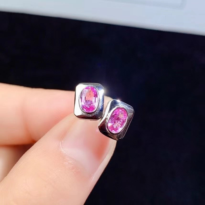 Silver earrings with pink gemstones held between fingers against a dark background