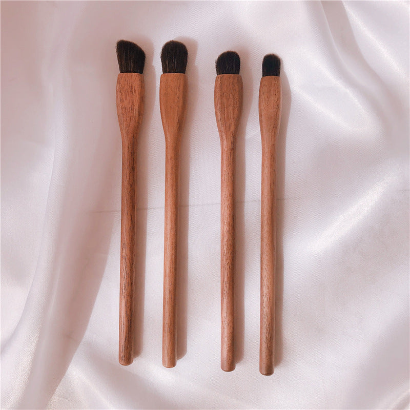 Four wooden makeup brushes with black bristles on a white fabric background