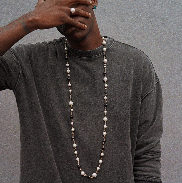 Person wearing a long pearl necklace against a gray background