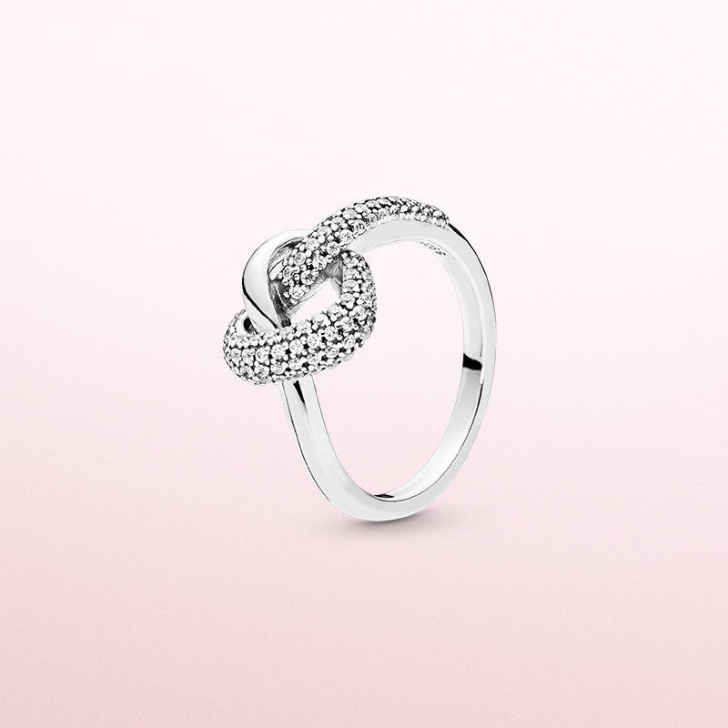 Silver ring with heart-shaped diamond design on a pink background