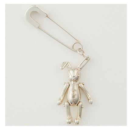 Silver safety pin with a small figure attached on a white background