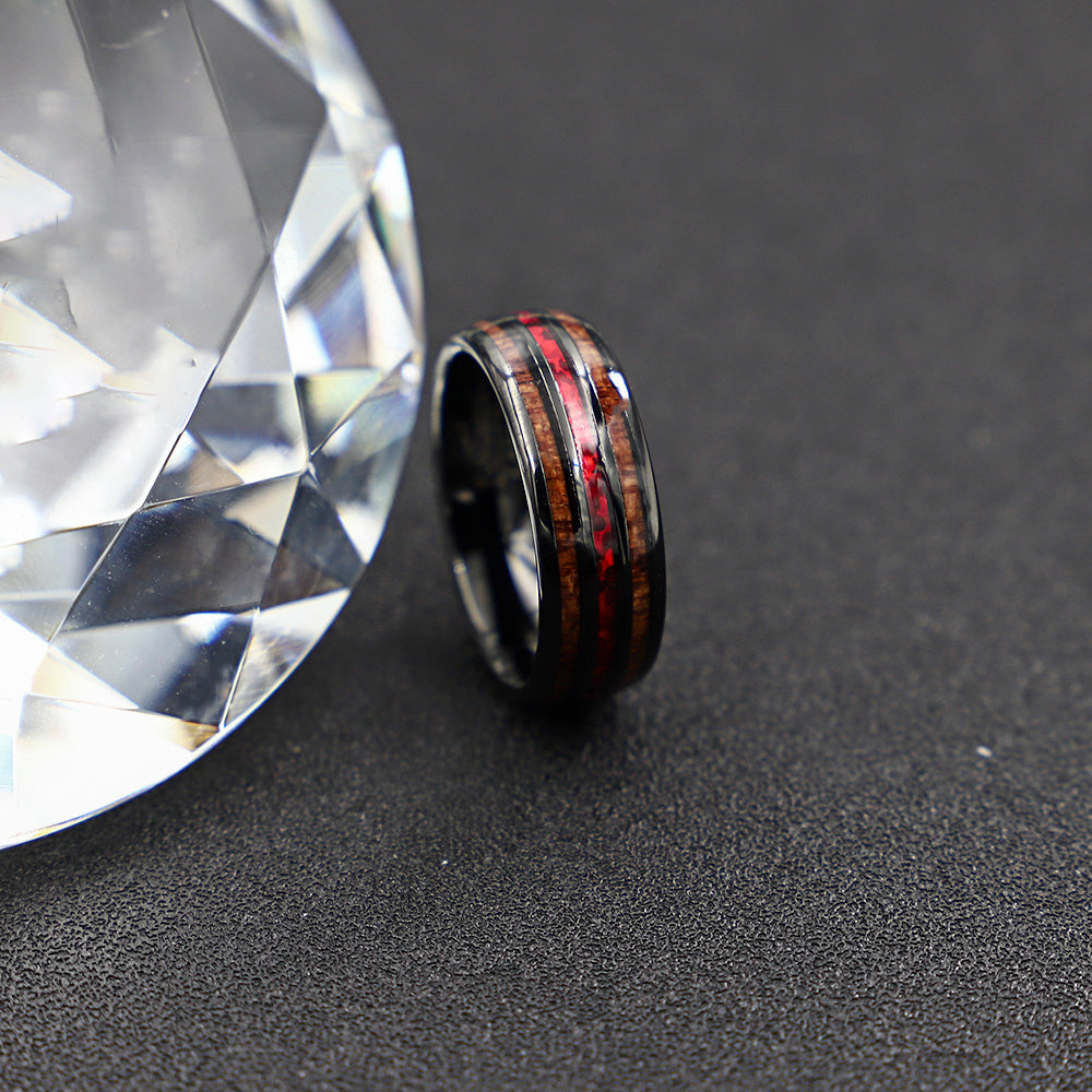 Wooden ring with red accents next to a large diamond on a dark surface