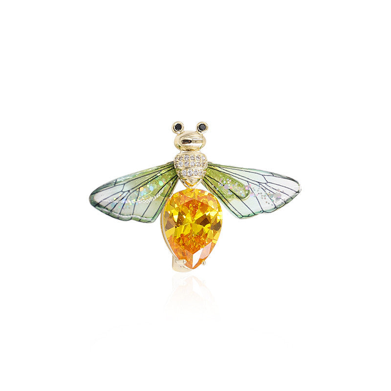 Jewelry item resembling a dragonfly with a yellow gemstone on a white background