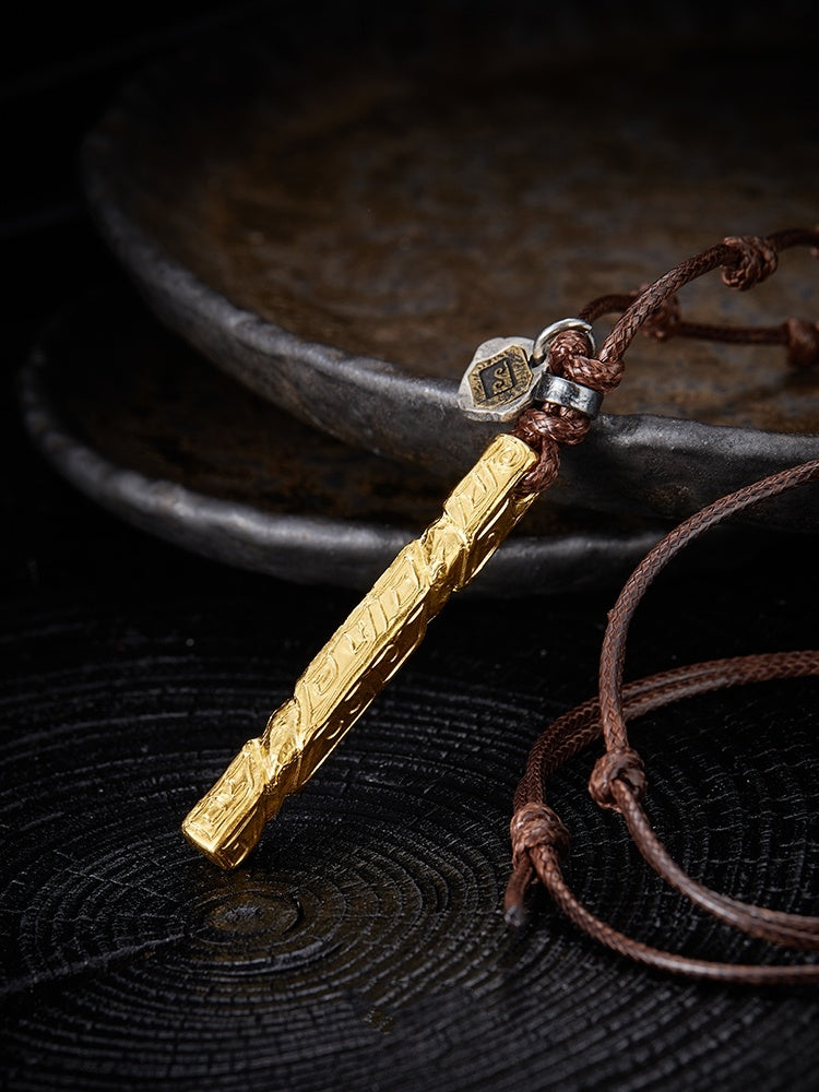 Gold pendant on a brown leather cord against a dark textured background