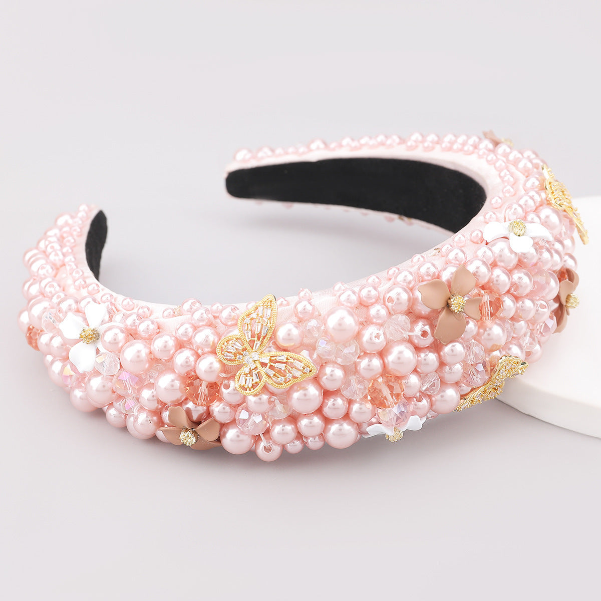 Pink beaded headband with gold accents on a light gray background