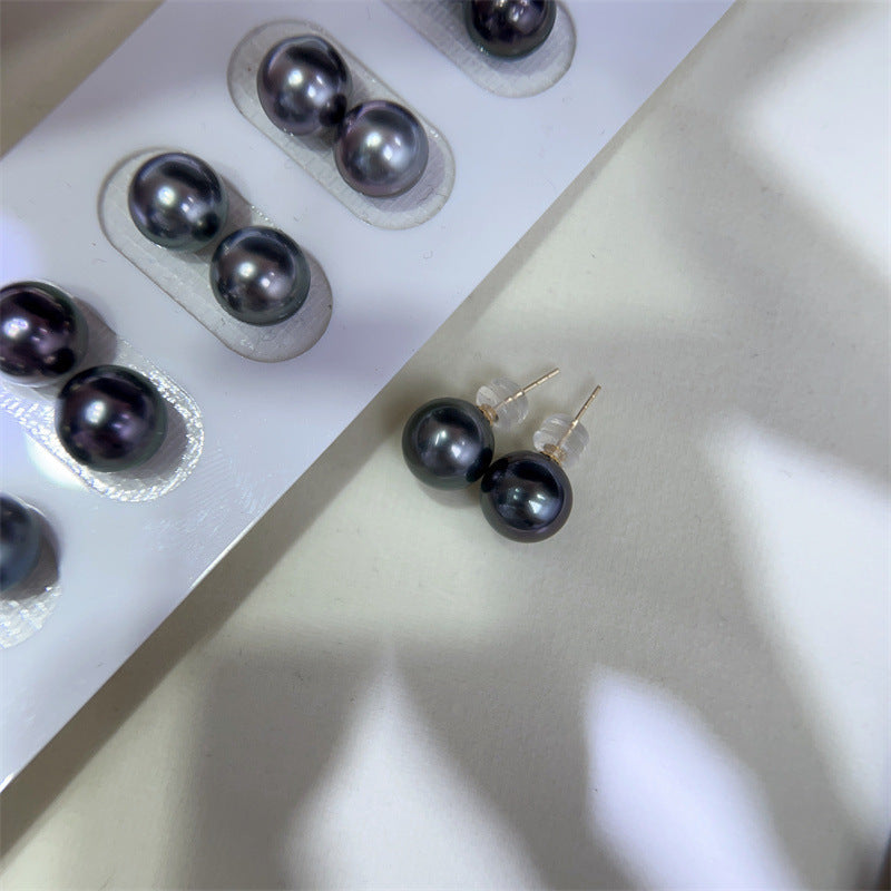 Black pearl earrings on a white surface with packaging in the background