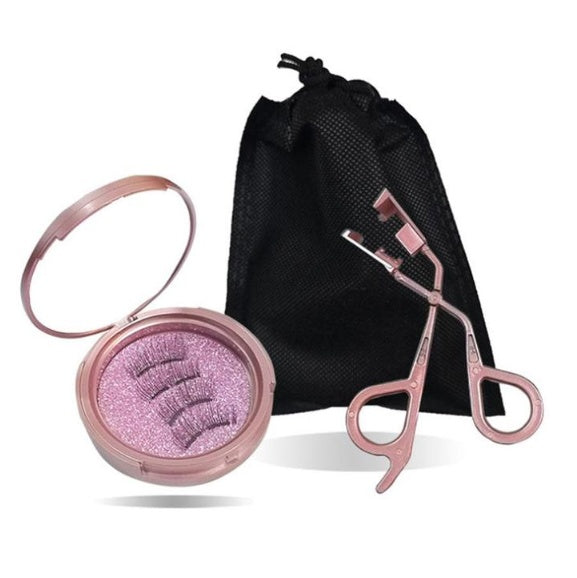 Makeup tool set with pink compact mirror, false eyelash applicator, and black drawstring bag on a white background