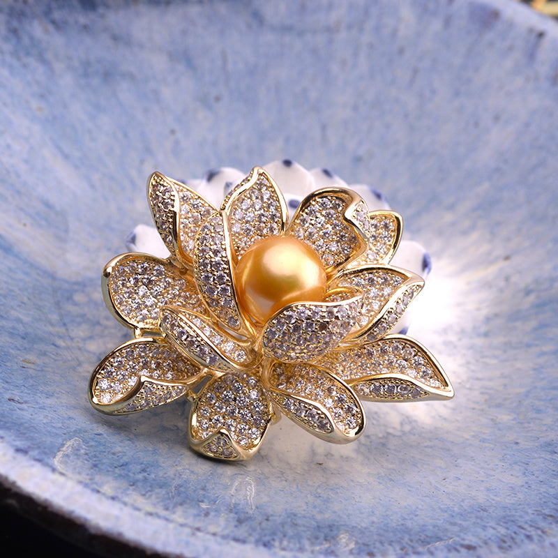 Gold lotus flower brooch with a pearl at the center on a blue stone background