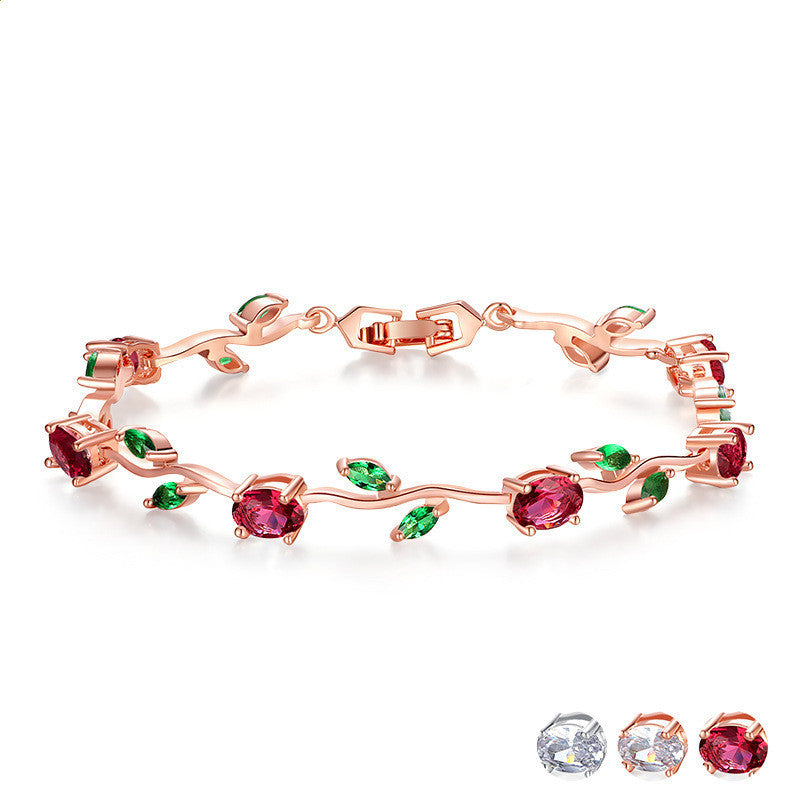 Rose gold bracelet with red and green gemstones on a white background