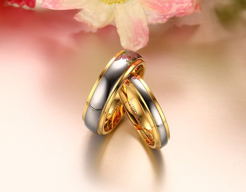 Two gold rings stacked on a soft pink background with a blurred flower.