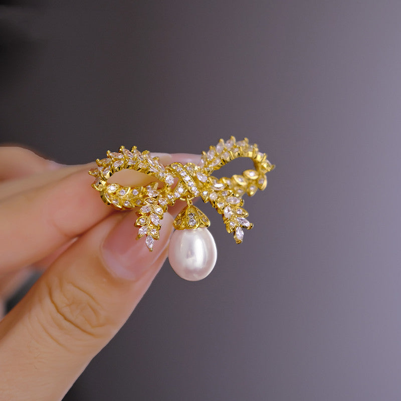 Gold bow-shaped brooch with a pearl held by a hand against a dark background
