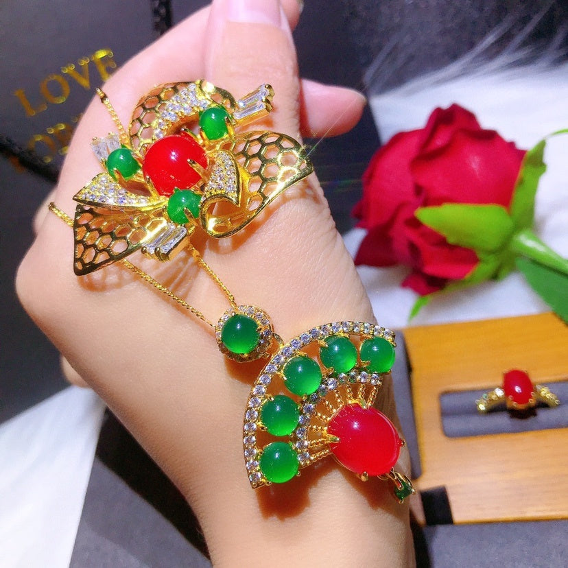 Gold ring with red and green gemstones on a hand, with a red rose in the background.