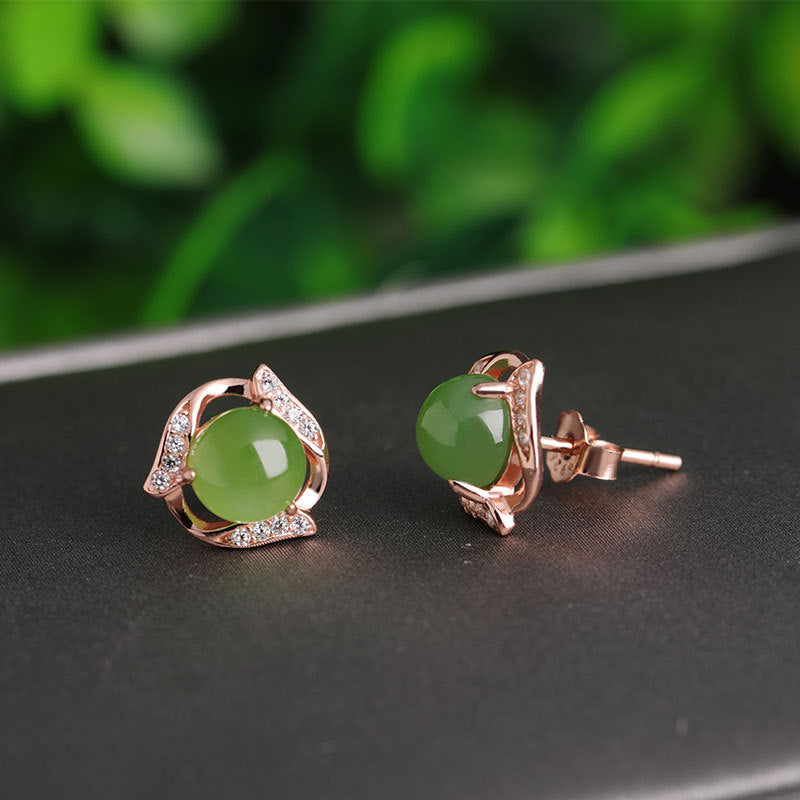 Rose gold earrings with green gemstones on a dark surface with a blurred green background