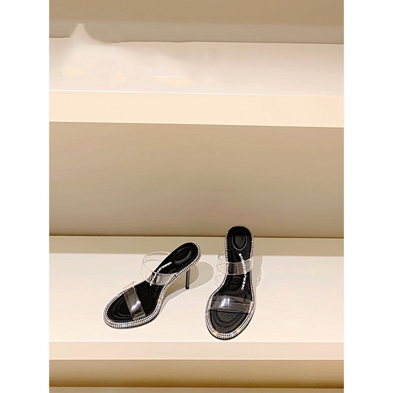 Black high-heeled shoes with clear straps on a light background