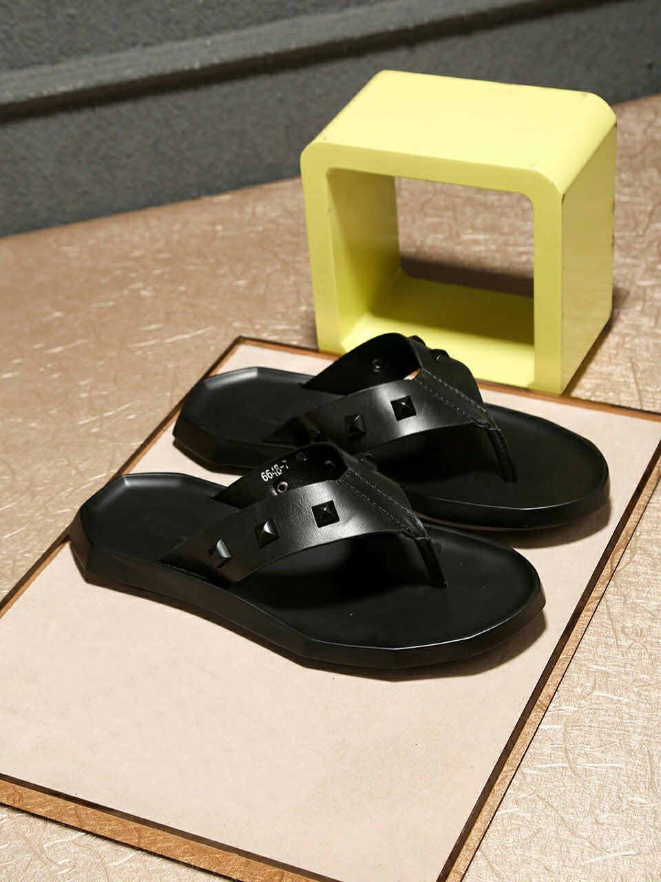Black sandals on a textured surface with a yellow box in the background