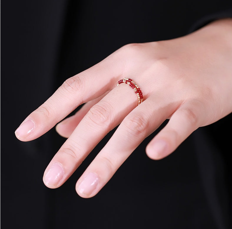 Hand wearing a red beaded ring on a black background