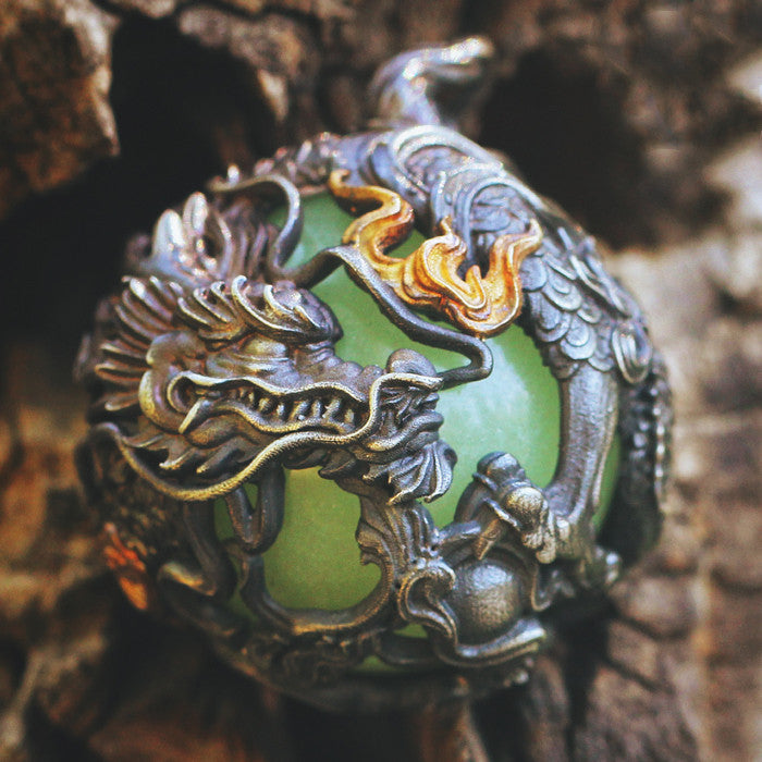 Decorative pendant with green gem and dragon design on a textured background