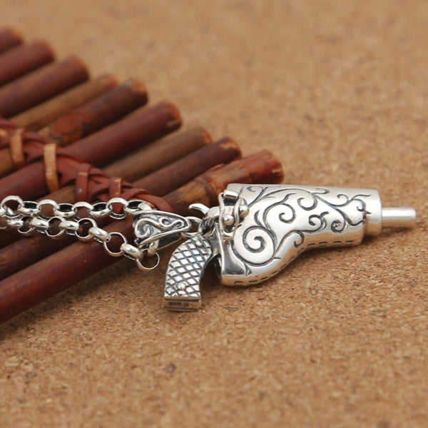 Silver revolver pendant on a chain against a brown background