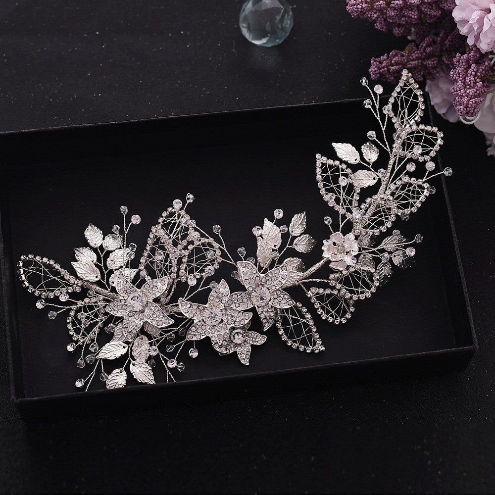 Decorative leaf and floral hair accessory on a black surface with flowers in the background