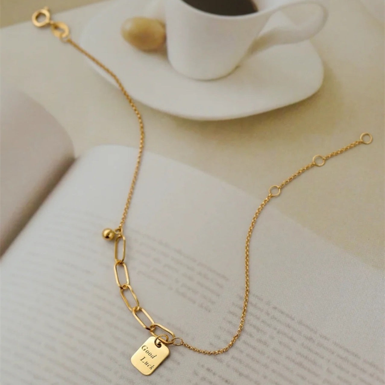 Gold bracelet with a tag on a surface with a cup of coffee in the background