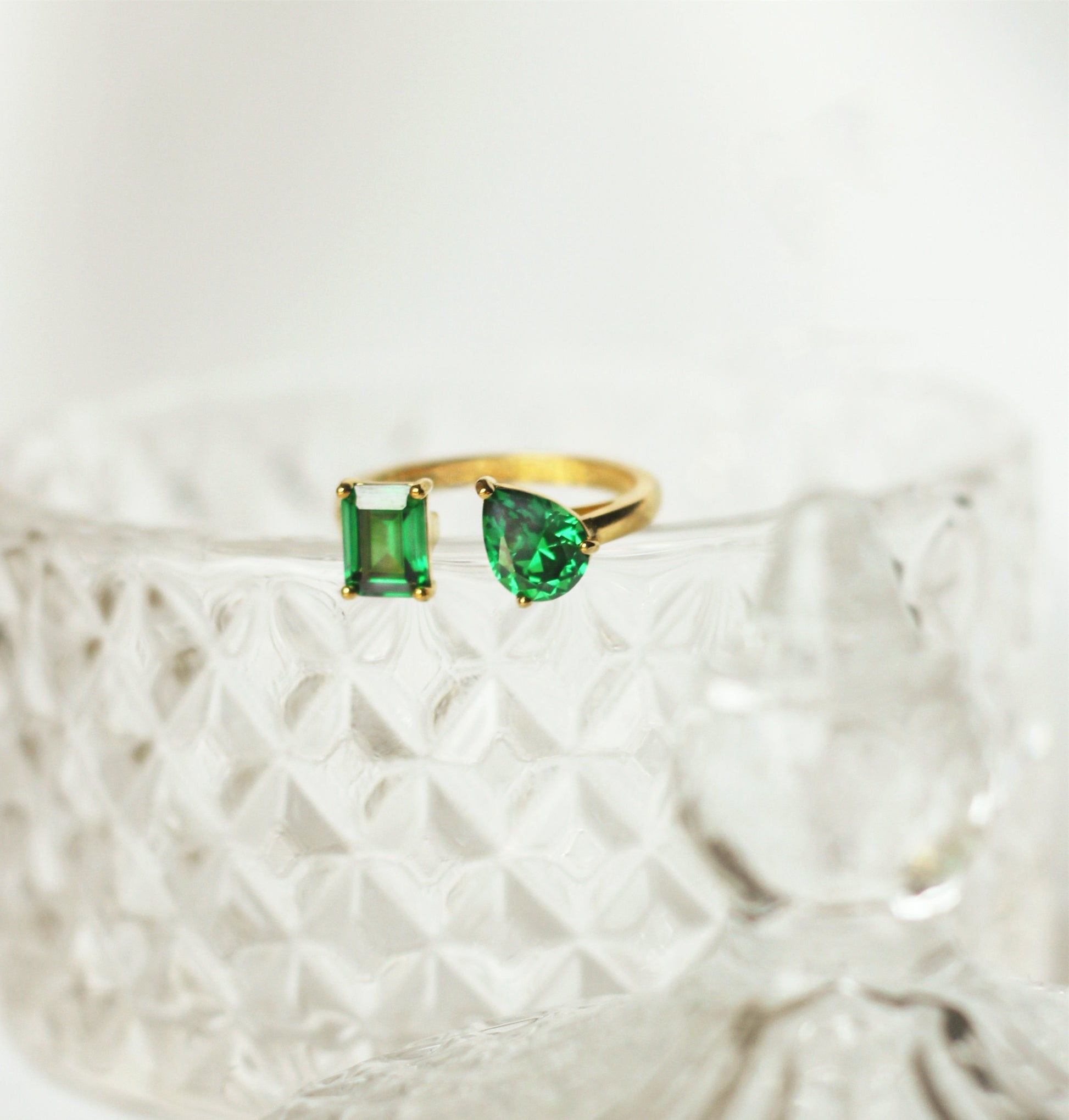 Gold ring with green gemstones on a textured white surface