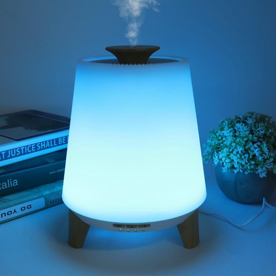 White diffuser emitting mist with a blue light on a surface next to books and a plant.