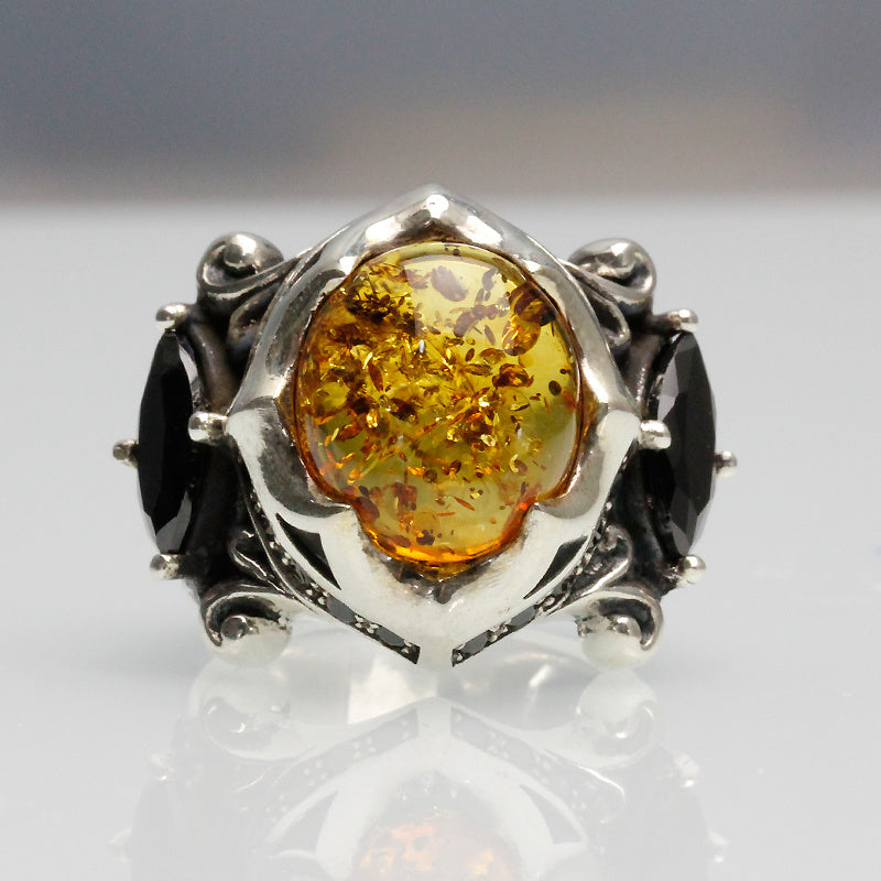 Ring with amber stone and black stones on a reflective surface