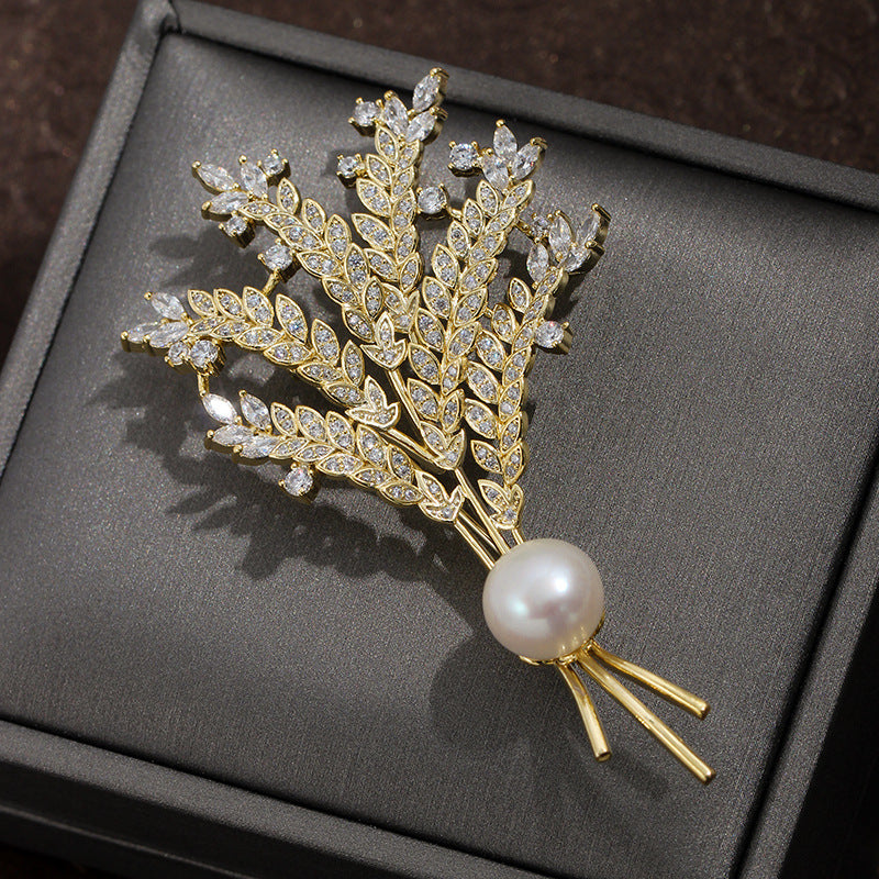Decorative brooch with leaf design and pearl on a gray surface