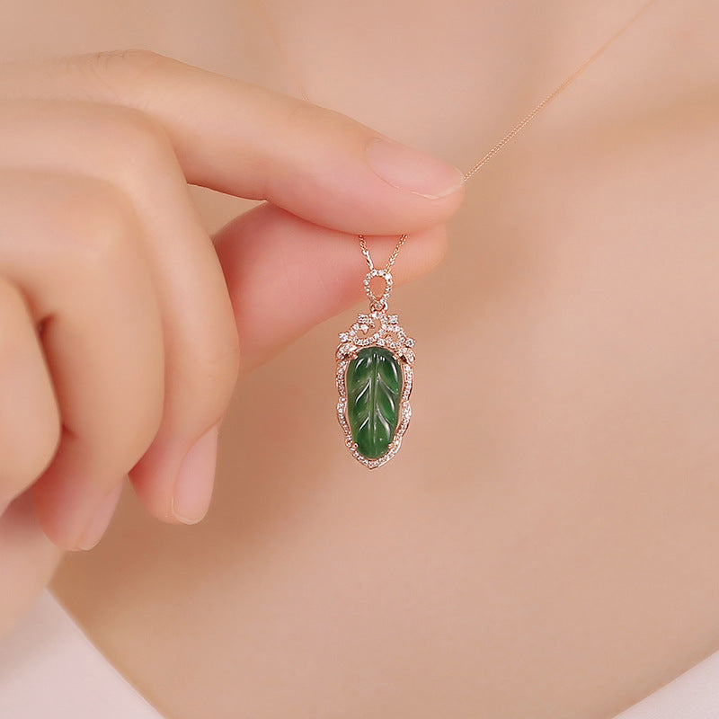 Hand holding a necklace with a green pendant against a soft background