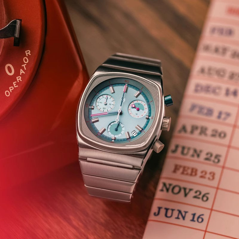 Silver watch with a blue face on a wooden surface next to a calendar