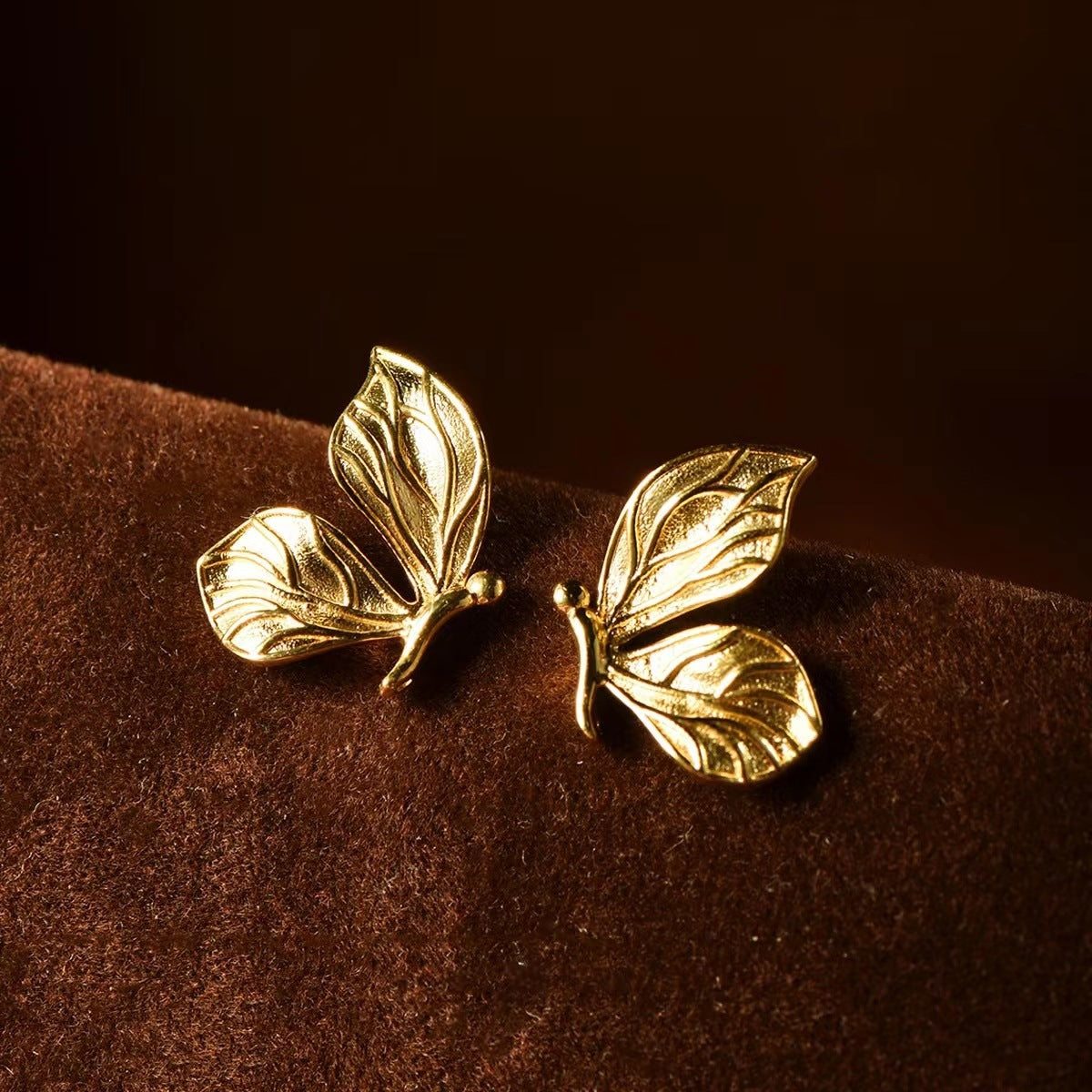 Gold butterfly earrings on a brown velvet surface