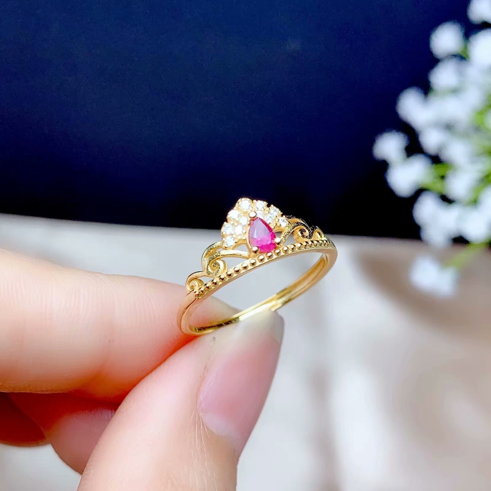 Gold ring with a pink gemstone held by a hand against a dark background