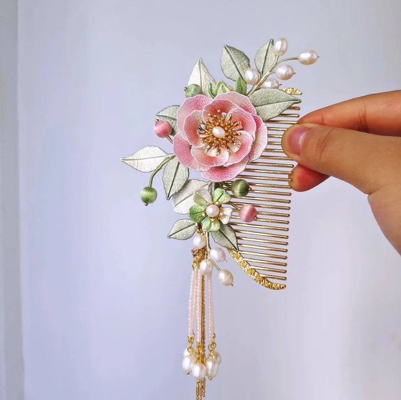 Decorative hair comb with floral design and pearl accents held by a hand against a light background