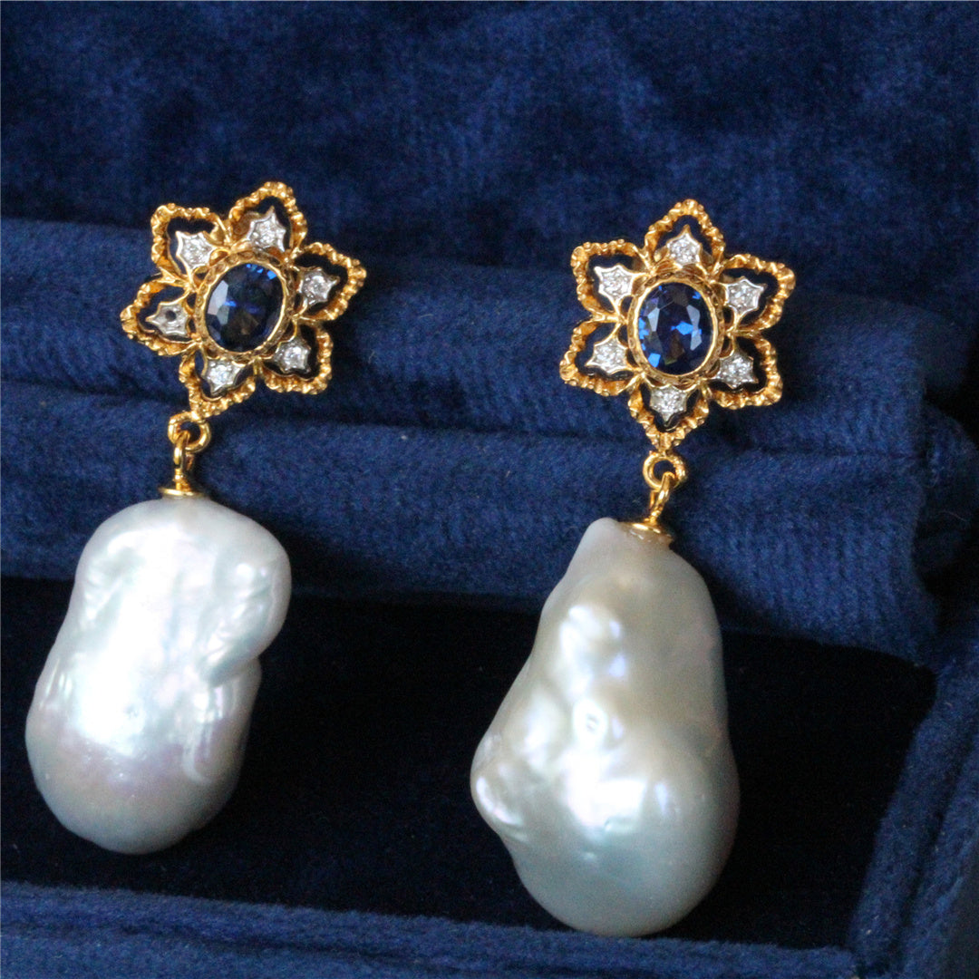 Pair of pearl earrings with gold and blue gemstone designs on a blue fabric background