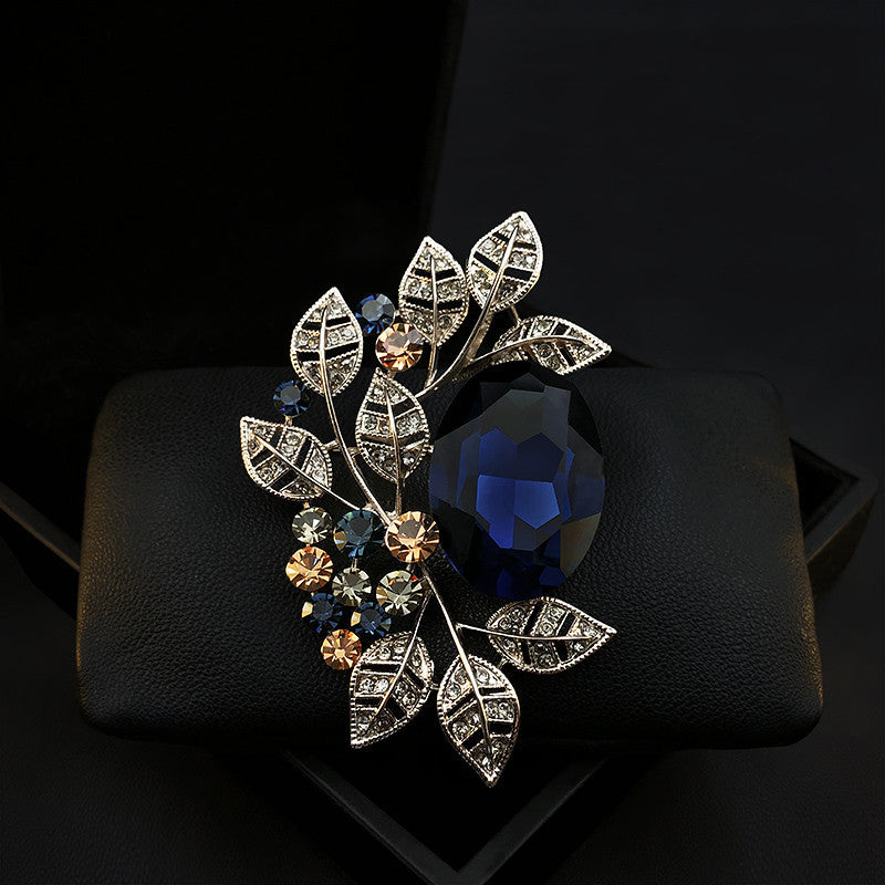 Decorative brooch with leaf design and gemstones on a black background