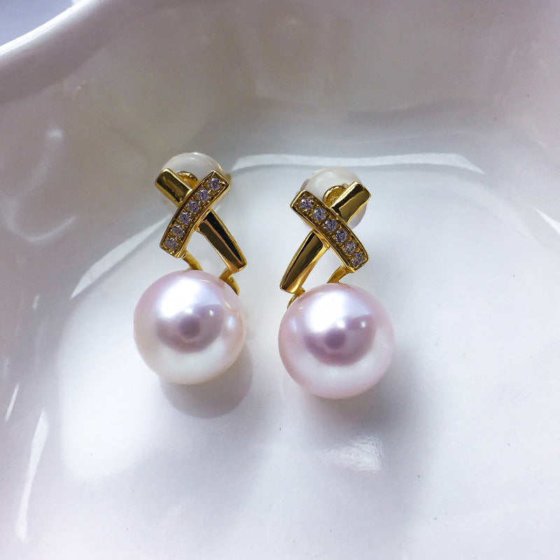 Pearl earrings with gold X-shaped designs on a white dish