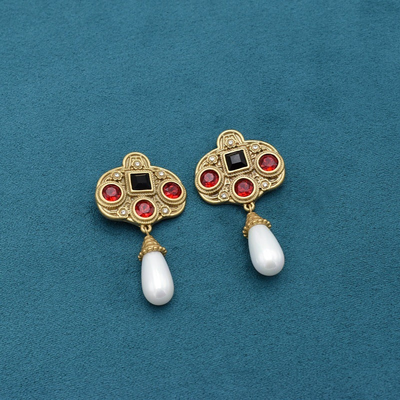 Gold earrings with red gemstones and white pearls on a blue background