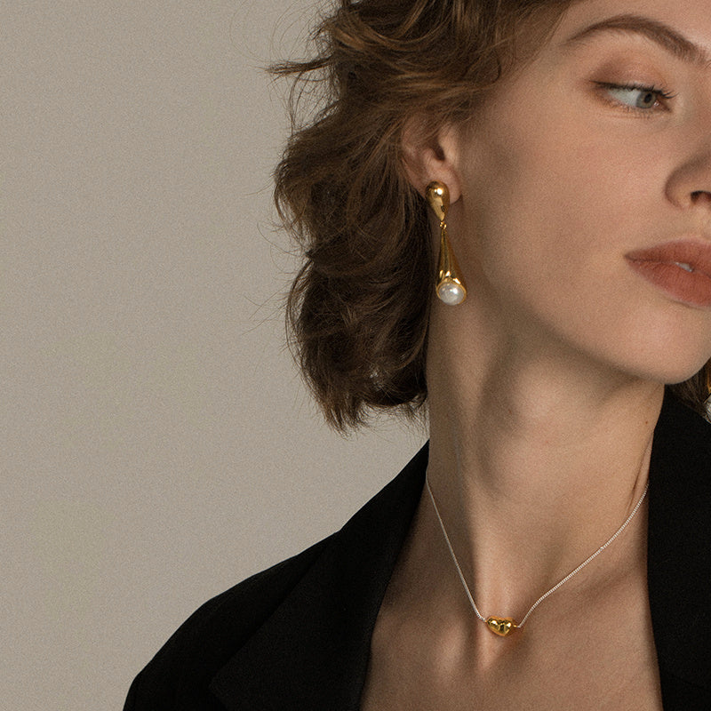Close-up of a woman wearing gold earrings and necklace against a neutral background