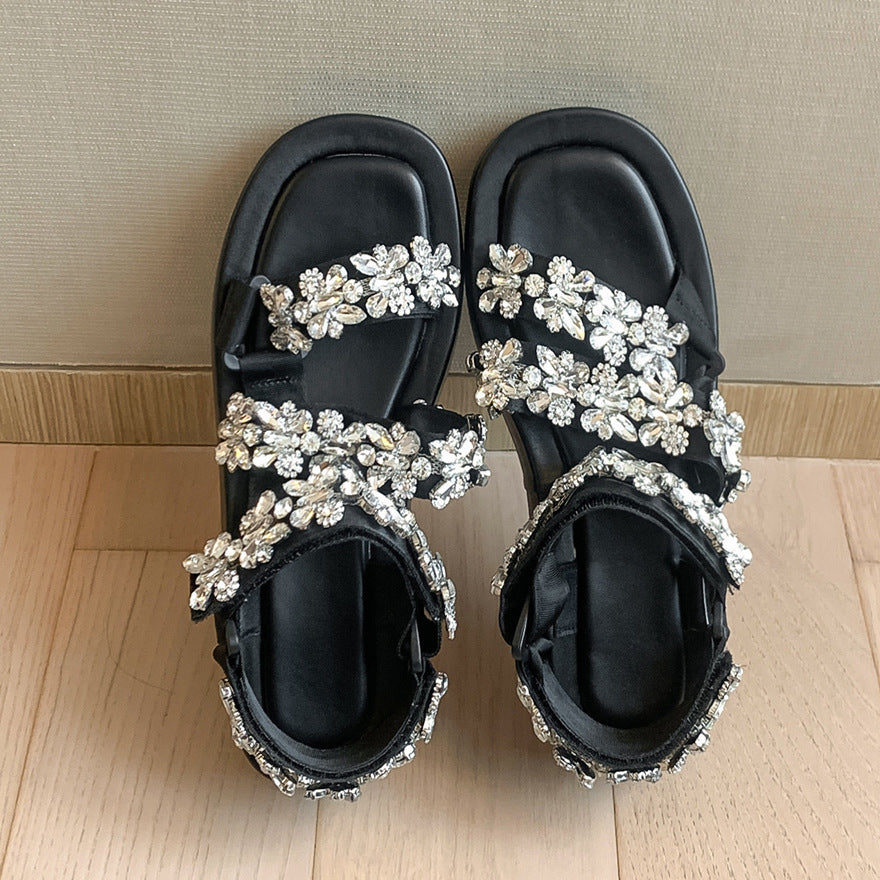 Black sandals with silver floral embellishments on a wooden floor.