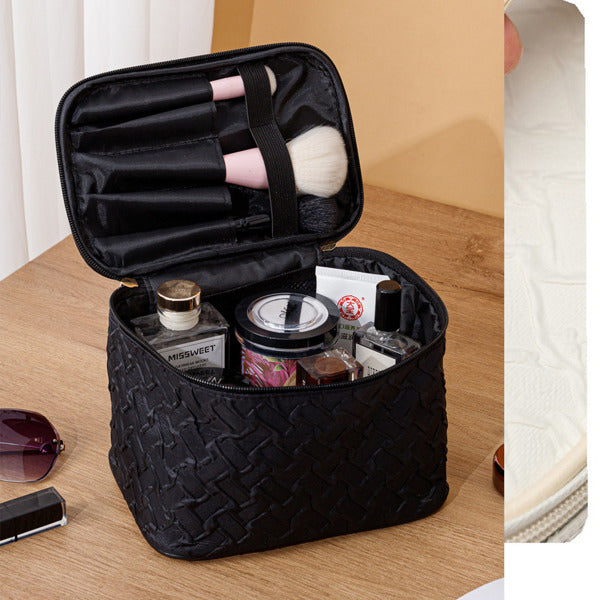 Black textured travel makeup bag with cosmetic items on a wooden surface