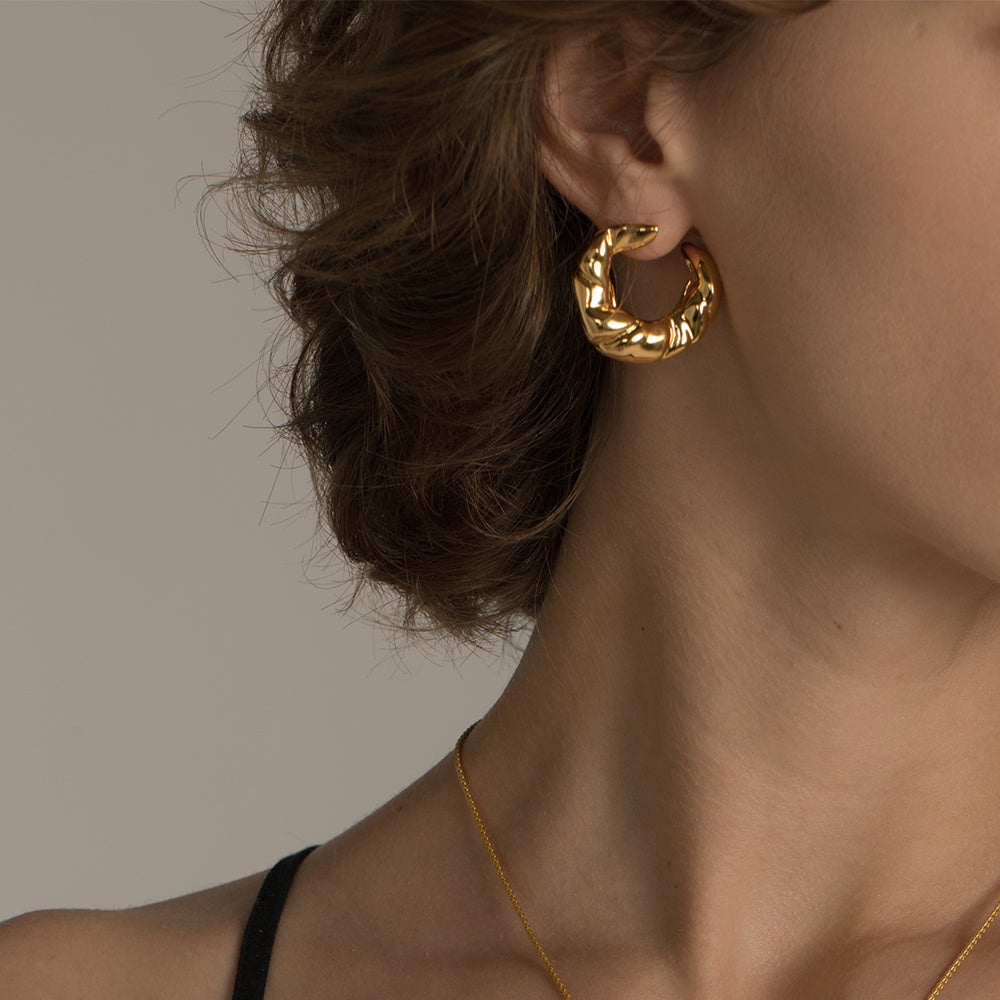 Gold hoop earring worn by a person with a neutral background