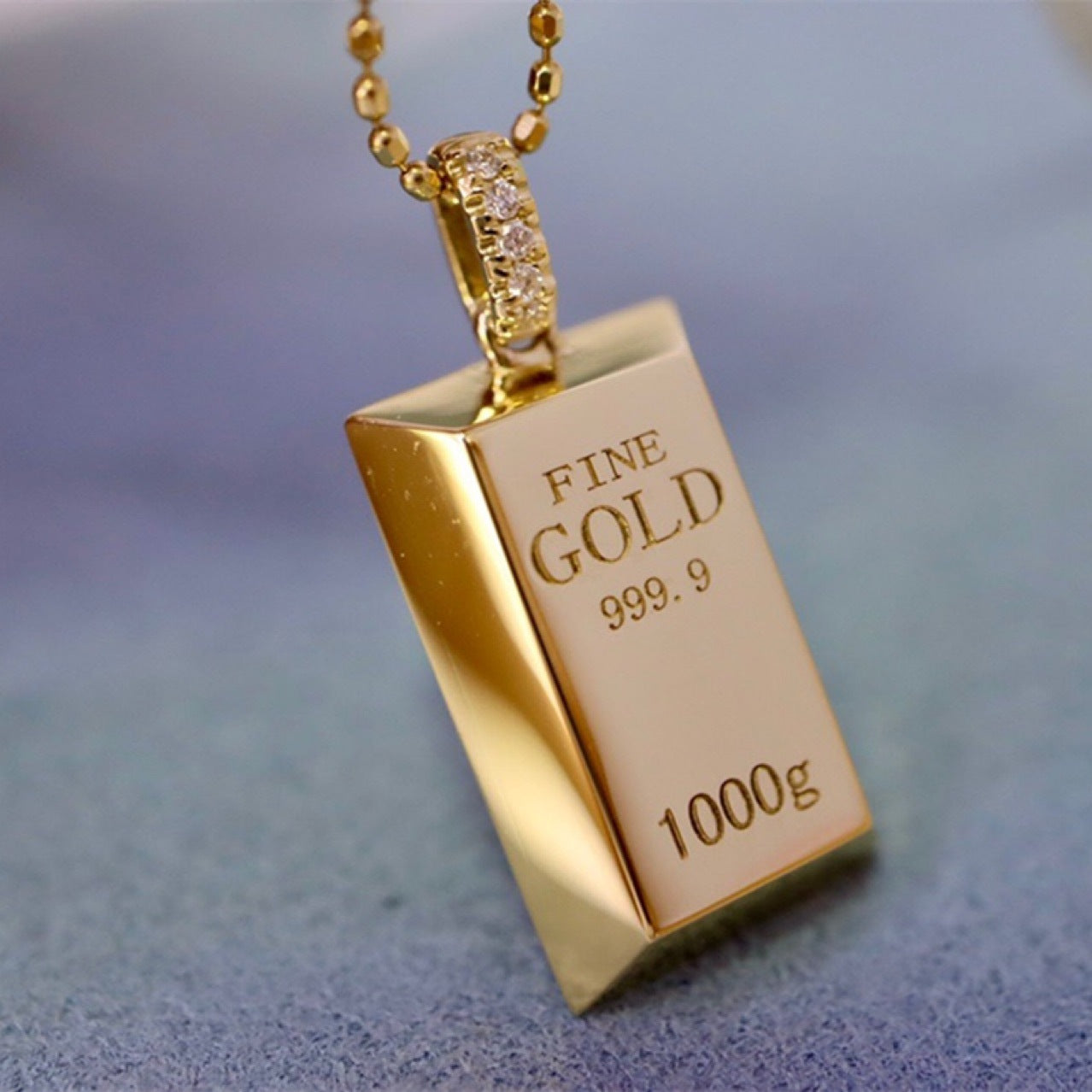 Gold pendant shaped like a gold bar with 'FINE GOLD 999.9' engraving on a blurred background