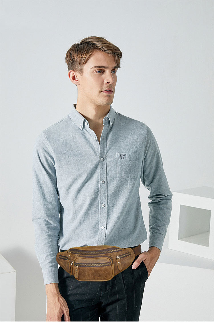 Man wearing a light blue button-up shirt and dark pants with a brown waist bag against a white background