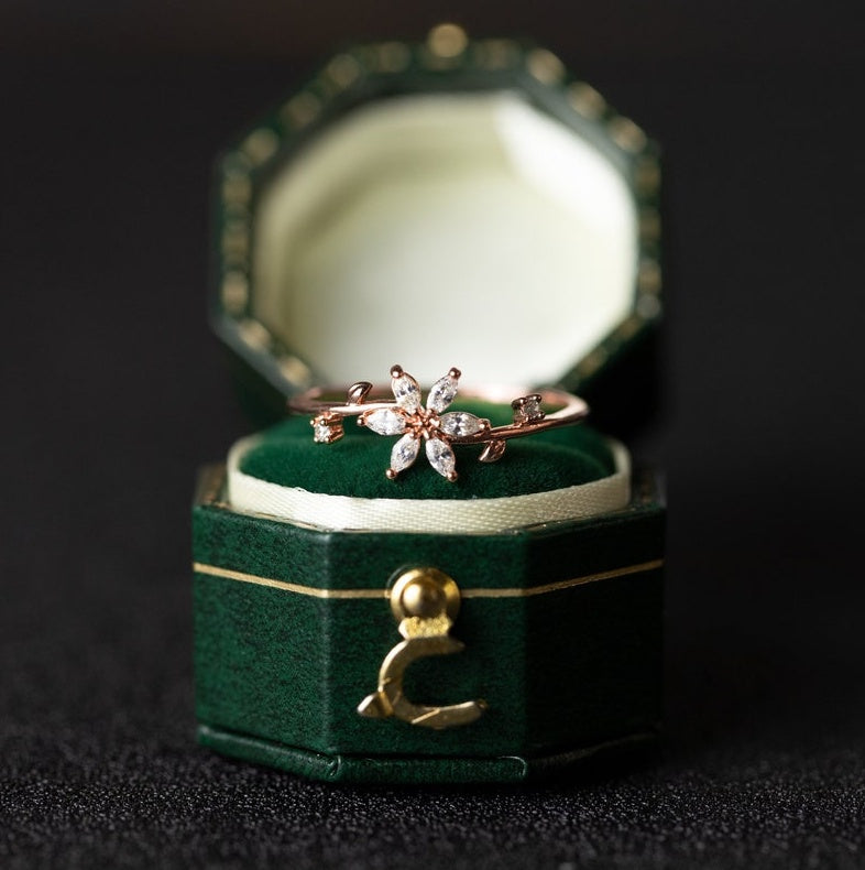 Gold ring with floral design in a green jewelry box on a dark background