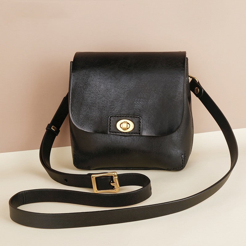 Black leather handbag with gold accents on a white surface and beige background