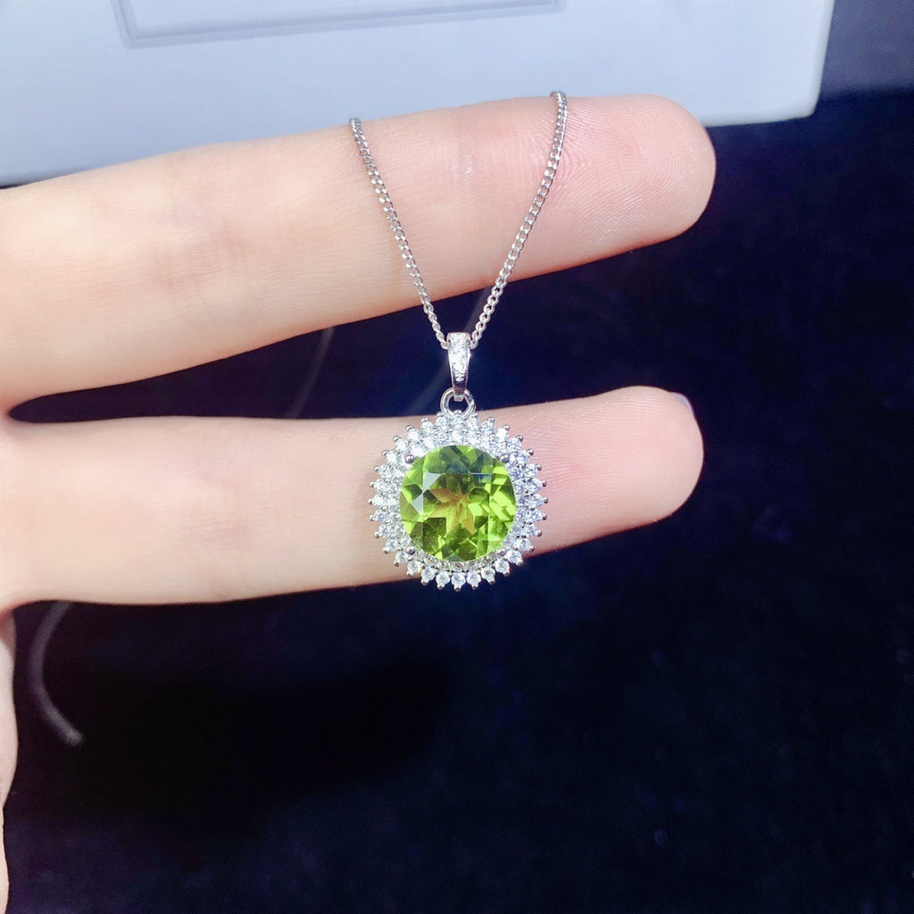 Green gemstone pendant on a silver chain held by a hand against a dark background