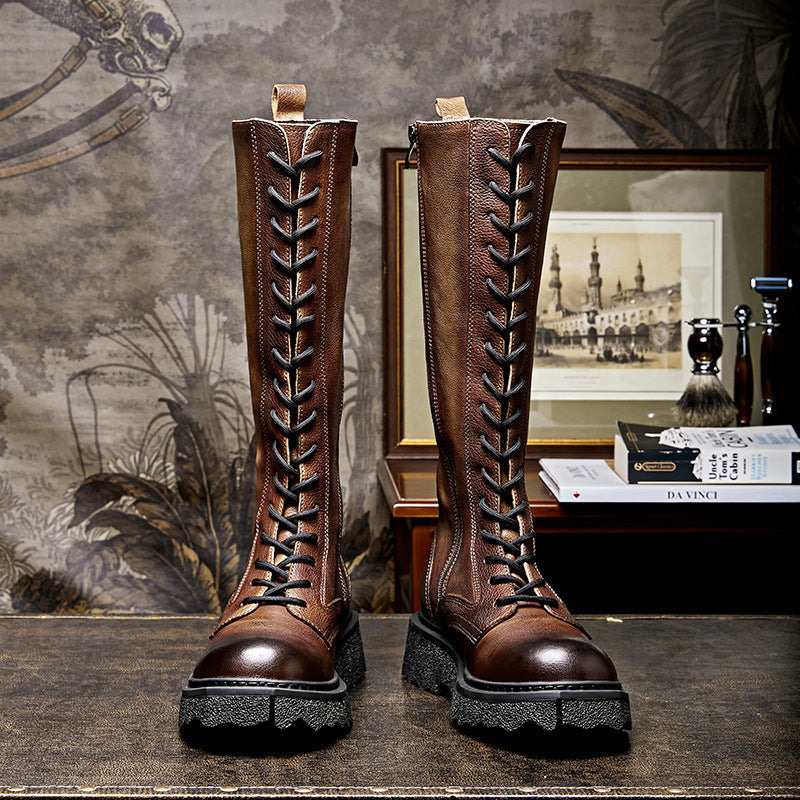 Pair of brown leather knee-high boots with lace-up design on a textured surface.