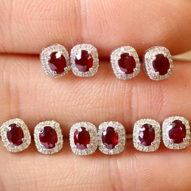 Pair of ruby earrings held between fingers on a light skin background