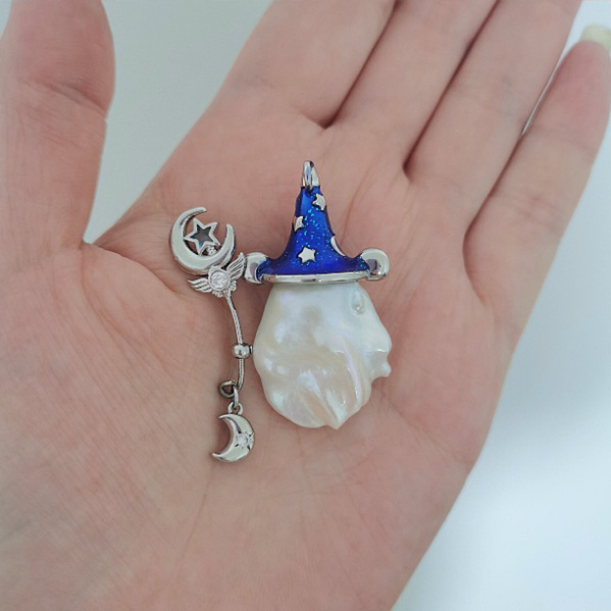 Pendant with wizard hat, moon, and star design held in a hand against a white background